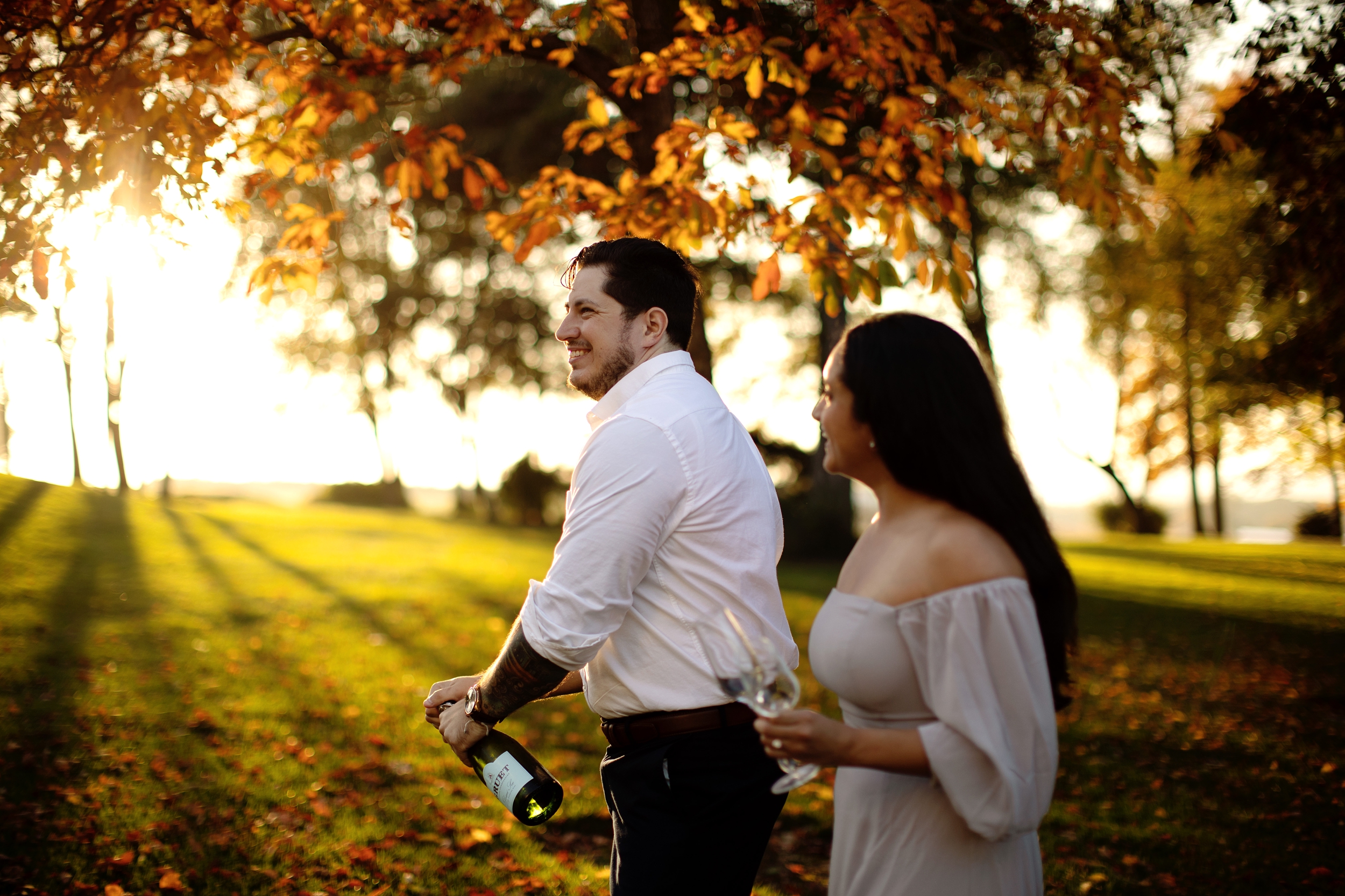 Engagement couple in the fall at Drumore Estate, Lancaster PA in a romantic off the shoulder lavender satin gown popping a bottle of champagne.